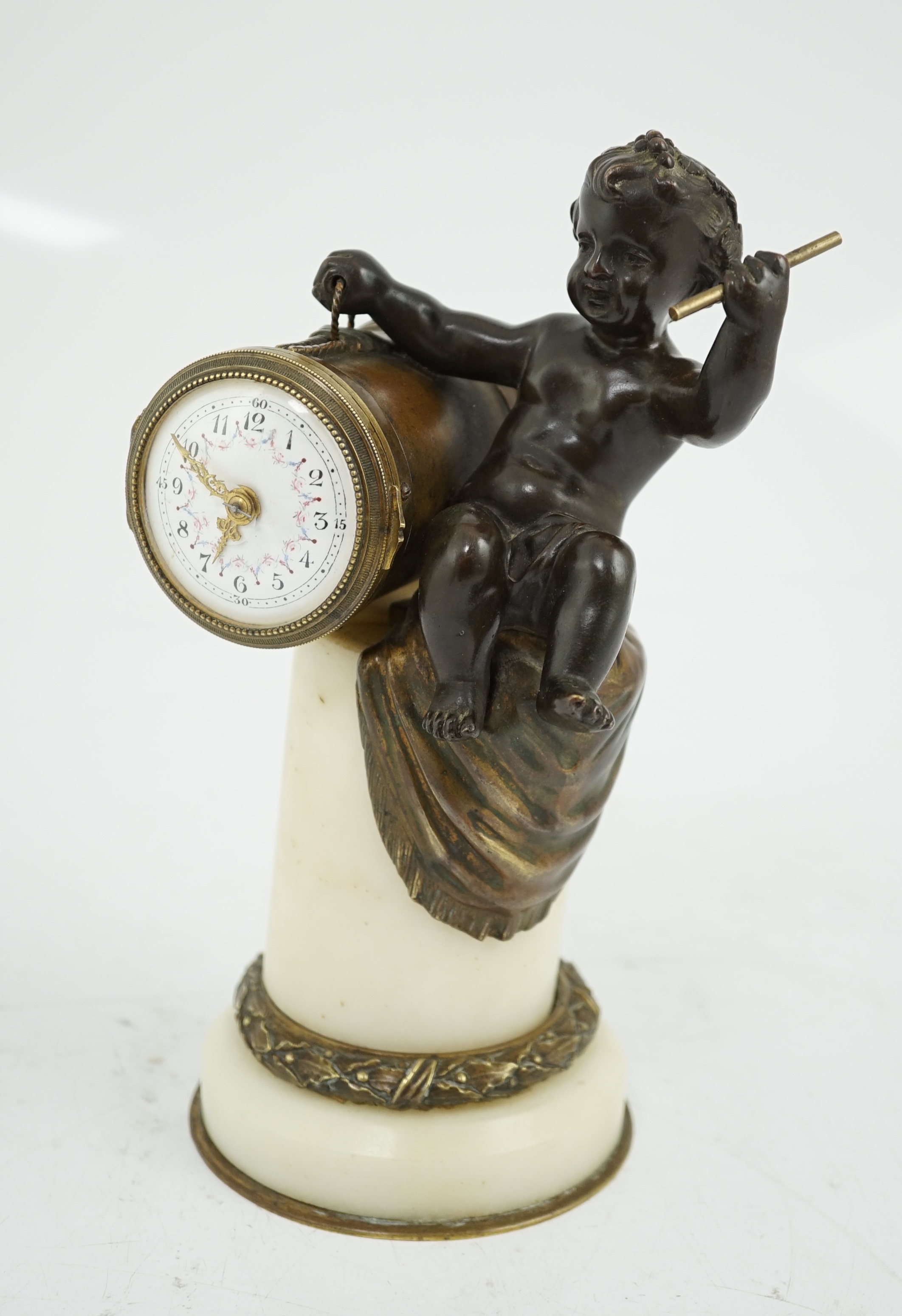 An early 20th century French eight day bronze and ormolu desk timepiece modelled as a putto banging upon a drum, with floral enamelled dial and white marble plinth, 12cm wide, 22.5cm high. Condition - good